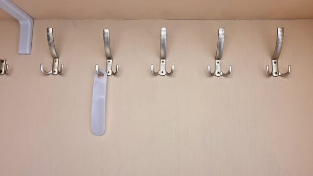 Row of metallic coat hooks mounted on a beige wall, with two hooks holding white hanging items, showcasing simple organization and practical storage in everyday spaces