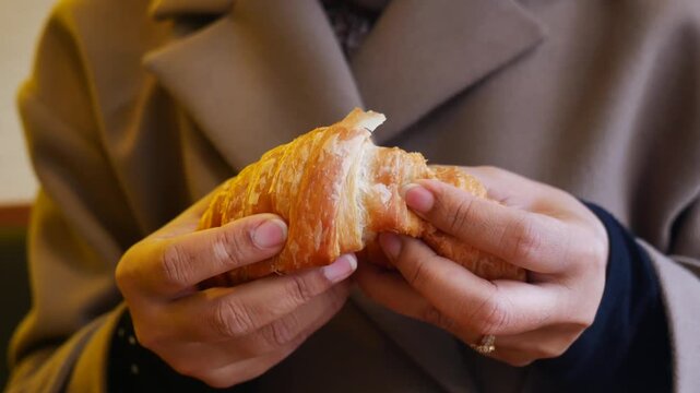 Woman hands breaking fresh flaky croissant in slow motion showing soft buttery layers and delicious texture