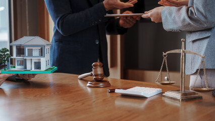 Real estate auction concept: gavel striking on model house atop laptop, with negotiators and scales...
