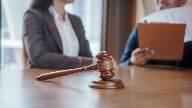 Real estate auction concept: gavel striking on model house atop laptop, with negotiators and scales of justice in background, symbolizing property law, sale, and contract agreement.