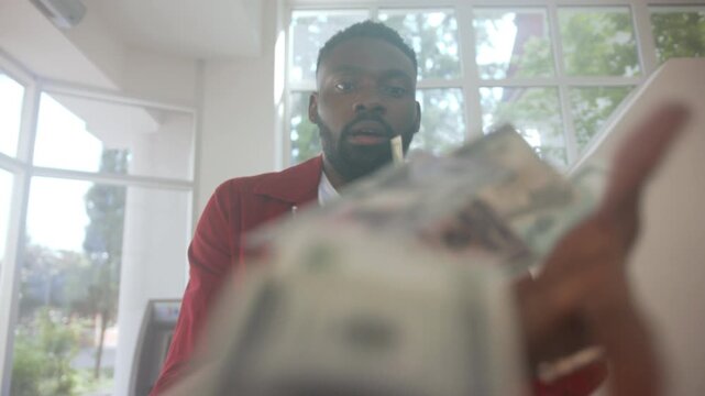 Man enthusiastically displays money indoors, Energetic entrepreneur poses with bills in bright home setting
