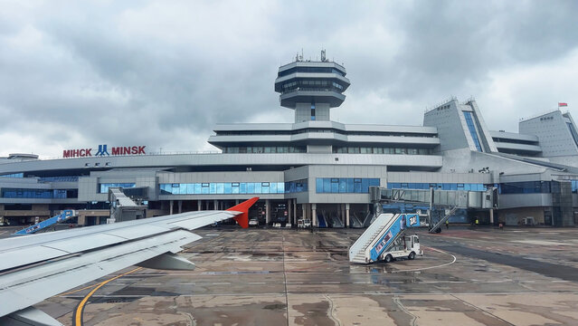 Minsk, Belarus - August 21, 2024: Airplane wing near passenger boarding bridge at minsk national airport terminal on a cloudy day