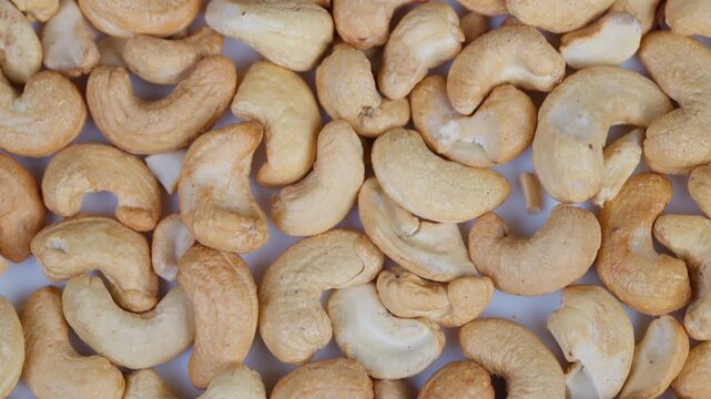 Detailed closeup view of toasted cashew nuts with shiny oil surface. Macro photograph capturing textured surface and overlapping arrangement of roasted cashew nuts