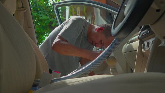 middle aged southeast asian man using vacuum cleaner to clean mpv car interior, warn morning light, natural background