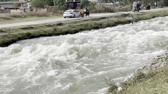 Fast flowing water in irrigation canal rural landscape with road and vehicles natural 