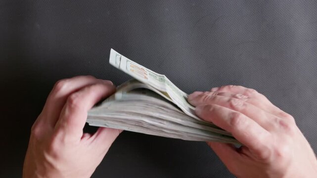 Person gathers a large stack of green and white paper currency. Scene evokes feelings of wealth, success, and financial gain indoors.