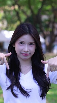 Young Thai University Student Smiling and Pointing Downwards in Outdoor Park