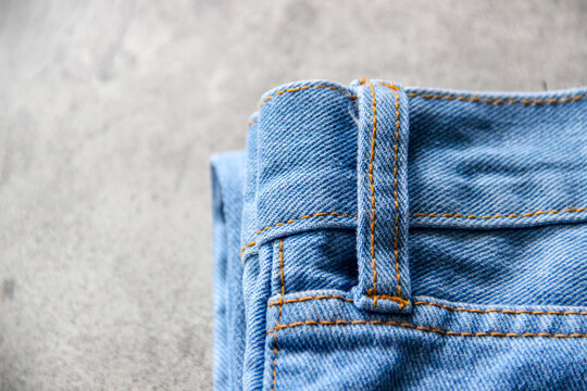 Close-up detail of blue denim jeans fabric with belt loop and orange stitching