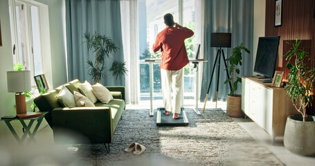 Freelancer, treadmill and phone call with man in home for communication, multitasking and chat. Remote worker, walking pad and connection with back of person in living room of apartment for contact © peopleimages.com