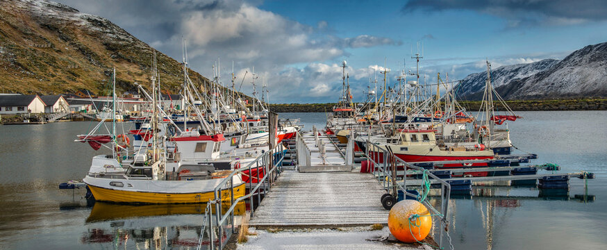 fishing boats of different colors moored on each side of a pontoon in harbor in norwegian village on Mageroya island, Nordland in Norway