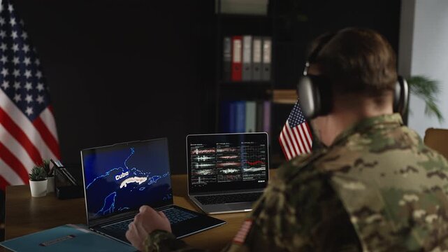 American service member in headset analyzing Cuba region intelligence on laptops