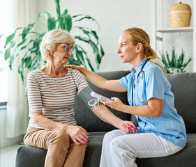Obraz premium Doctor or nurse caregiver with senior woman using blood pressure tool at home or nursing home