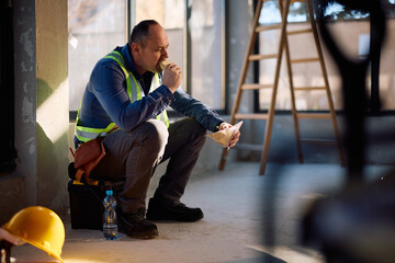 Mature worker enjoying in sandwich on lunch break at construction site.