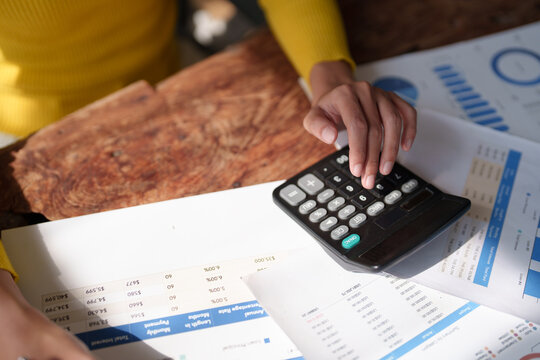 Hands using a calculator to process financial data and accounting reports on a wooden desk, surrounded by paperwork, spreadsheets and charts for budgeting and analysis