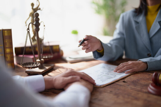 Lawyer discussing legal advice with a client, pointing to important sections of a document during a consultation, with scales of justice and law books on the rustic wooden table