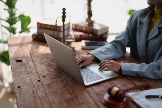 Legal professional working on laptop at rustic wooden desk with law books, scales of justice, and a gavel, symbolizing modern legal practice and research