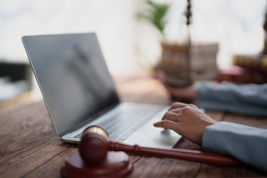 Person using laptop with judge's gavel on wooden desk, symbolizing online legal services, digital law, remote consultations, legal tech, document review and court technology