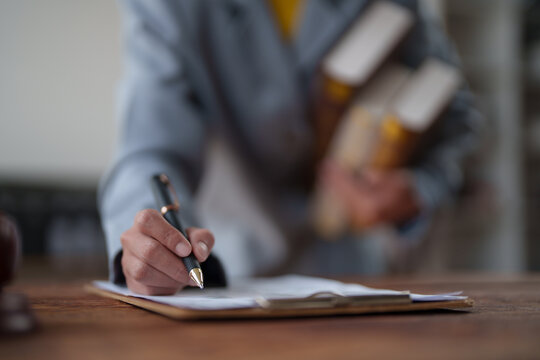 Business hand holding a pen and writing signature on a contract document placed on a clipboard, while also carrying law books, symbolizing legal expertise, agreement, and official paperwork