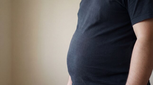 Close-up of a mans belly, showcasing a prominent beer gut and the effects of an unhealthy lifestyle.