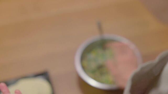Close-up of hands wrapping gyoza filling in dumpling wrapper on wooden table