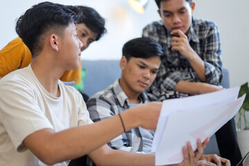 Fototapeta premium Four Young Asian Men Discussing Paperwork and Collaborating on Project in Bright Indoor Setting