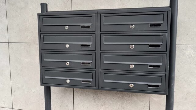Modern grey metal mailboxes for residential apartment building. Horizontal cinematic pan of contemporary post boxes on architectural facade background.