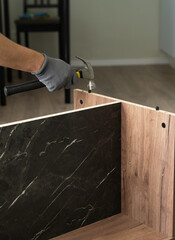 Hands assemble wooden nightstand using hammer. Installing furniture dowel pin. Process of assembling furniture