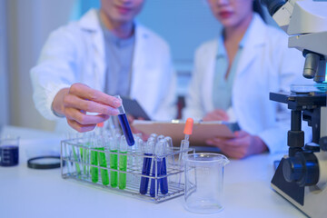 Fototapeta premium Scientists place a blue liquid sample into a test tube rack while documenting results, highlighting careful handling and accuracy in laboratory research.