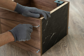 Hands assemble wooden shelf using screwdriver. Process of assembling furniture. Furniture assembler installs fasteners