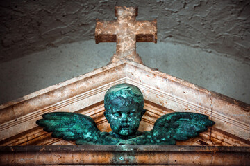 Naklejka premium Winged Cherub Statue Below Stone Cross