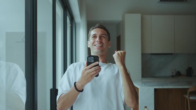 Man looks at smartphone and celebrates success with joyful yes gesture This moment shows success achievement and success feeling from good news reward or winning result in modern everyday life at home