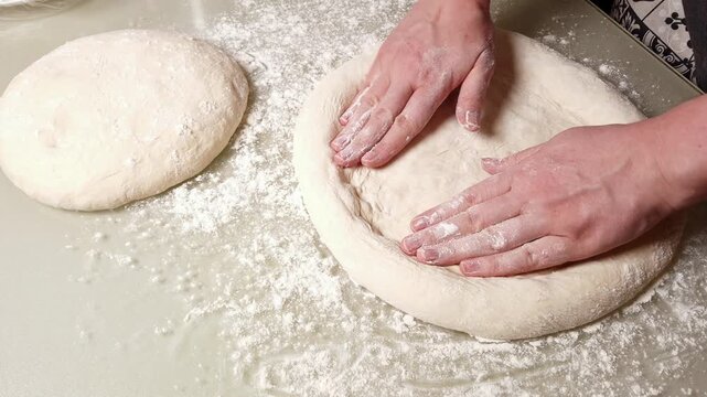 Close-up view of hands gently stretching and shaping raw pizza dough on a lightly floured countertop, preparing for a delicious meal