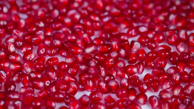 Magnified photograph emphasizing vibrant pomegranate arils and water droplets. Closeup macro image displaying colorful pomegranate seeds with shiny reflections and juicy texture