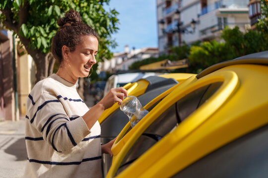 Woman recycling plastic bottle in yellow bin on a sunny street