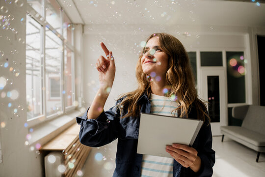 Smiling woman in studio holding tablet and reaching for bubbles