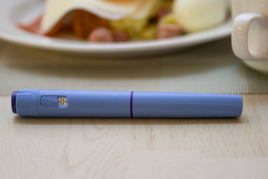 ozempic pen semaglutide injection blue medical device on wooden table with healthy food blurred in background for diabetes management and weight loss concept of healthcare, medicine, pharmacy