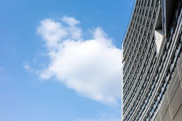 A modern high-rise office building stands tall against a vibrant blue sky with soft white clouds, showcasing minimalist urban architecture and contemporary glass facade design. © Anton Kustsinski