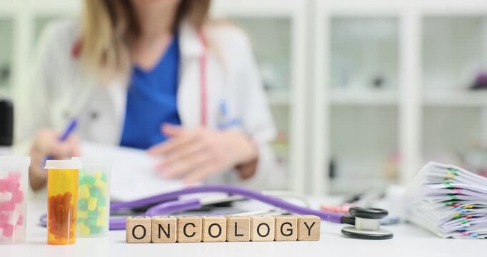 Miniature wooden cubes on table form word Oncology near medications. Woman doctor reviews clinical notes and prescribes chemotherapy phases to patient