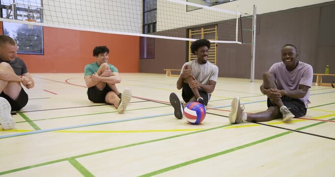 Diverse male players warming in gym in kit after fourth joining, prepping to play with volleyball