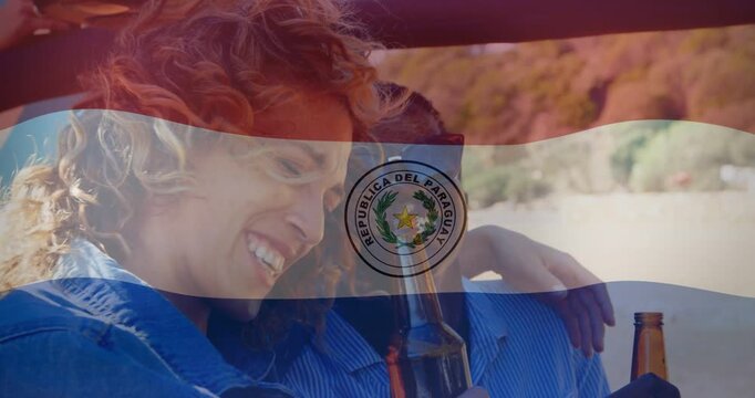 Vertical video: Cam pulling back revealing duo leaning on beach sharing beer, denim, Paraguay flag