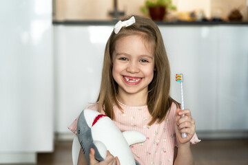 Portrait of little happy toothless girl with toothbrush looks at camera and laughs. Childrens oral hygiene. Baby milk teeth change