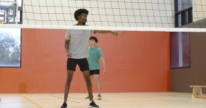 Diverse men playing in gym, attacker spiking ball over net, African American man blocking to defend