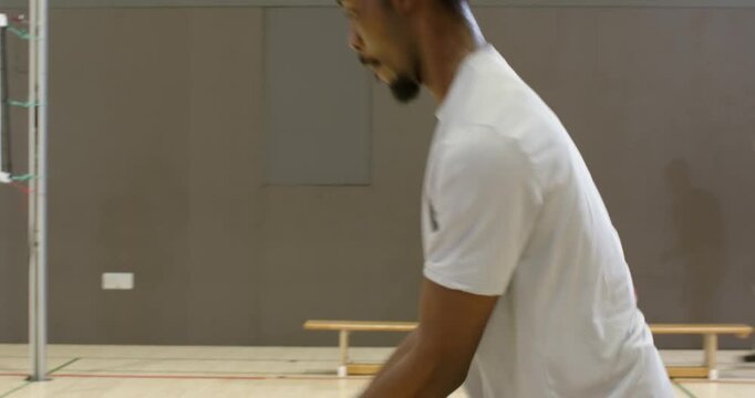 Diverse men practicing in gym with server tossing red white blue volleyball as tall player bumping