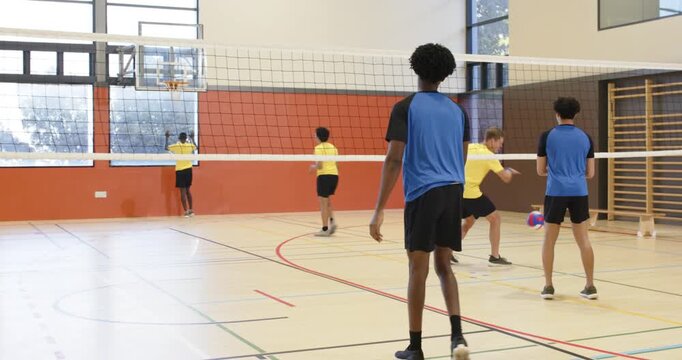 Yellow player initiating overhead set, African American man moving to net in gym, spiking for point