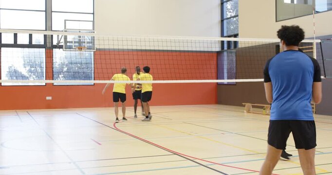 Adult male in blue jersey jumping to block yellow serve over volleyball net in school gym