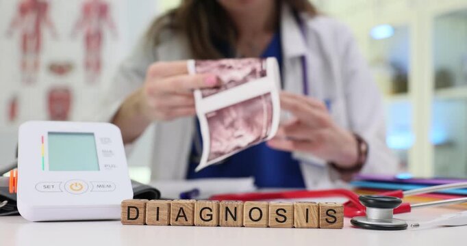 Wooden blocks spell word Diagnosis near ultrasound prints and blood pressure monitor. Doctor woman holds scan results reviewing patient findings