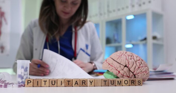 Wooden blocks spell phrase Pituitary Tumors near brain model and medicine vial. Doctor woman sorts documents flagging endocrine imaging results