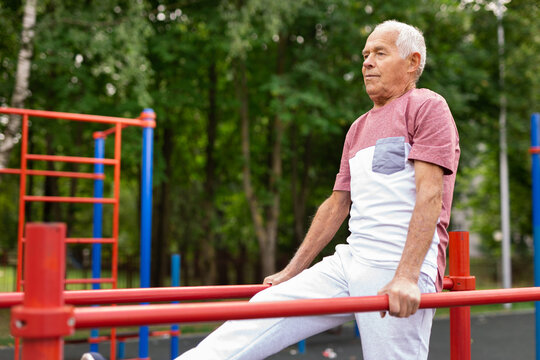 Elderly sportive man doing parallel bars exercise in park