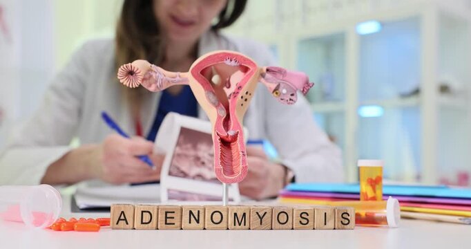 Row of wooden blocks spells word Adenomyosis near uterus model and ultrasound print. Gynecology doctor reviews scan writing treatment plan for patient
