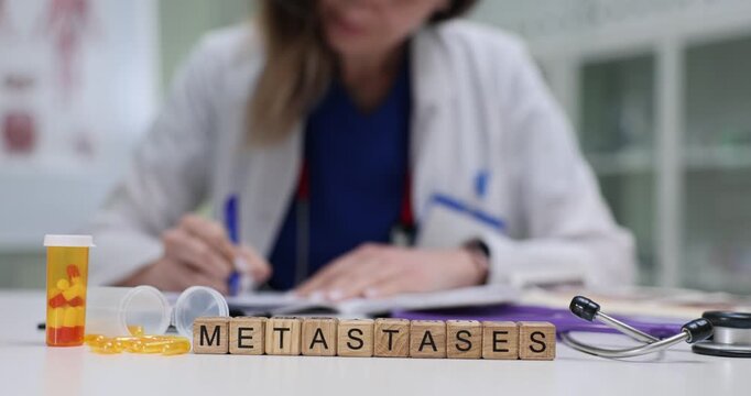 Woman oncologist reviews previous treatment responses and writes detailed chemotherapy plan for patient. Wooden cubes arranged to form word Metastases